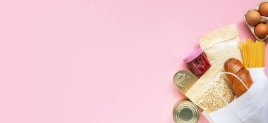 Pembe arka planda bağış yiyecekleri ve fotokopi alanı. Pankart. Model yap. Pirinç, konserve yiyecek, yulaf gevreği, yumurta, reçel, makarna. Yiyecek bağışları ya da yemek servisi konsepti. Covid 19 karantinası sırasında online alışveriş