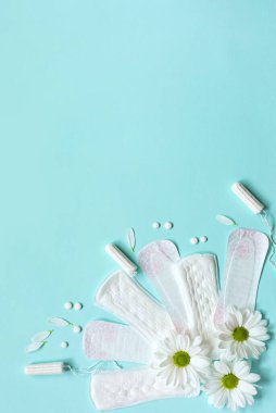 Adet tamponları, tamponlar ve mavi arka planda beyaz çiçekler. Dikey. Regl döngüsü, hijyen ve koruma kavramı. Metnin için alanı kopyala. Düz la