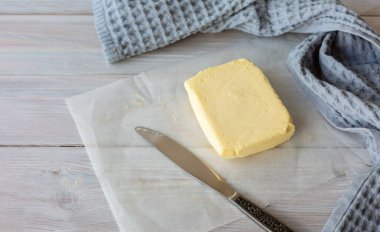 Parşömen üzerinde lezzetli sütlü tereyağı, bıçak ve ahşap masa üzerinde gri peçete. Kapat..