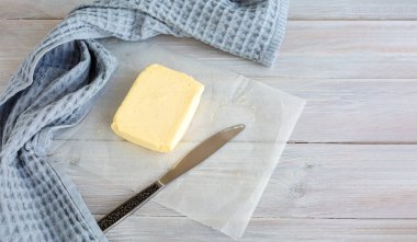 Parşömen üzerinde lezzetli sütlü tereyağı, bıçak ve ahşap masada gri peçete. Seçici odaklanma. Metnin için alanı kopyala. Üst görünüm. 