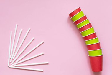 Kağıt bardaklar ve pembe arka planda beyaz pipetler. Açık yeşil ve kırmızı bardakları koyun. Üst Manzara. Kavram - çevre dostu, sıfır atık, plastiksiz. Metnin için alanı kopyala. Düz la