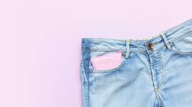 Pembe arka planda açık mavi kot pantolon cebinde regl pedi. Kadın hijyeni. Kritik günlerde kadınlar için hassas koruma, jinekolojik adet döngüsü. Uzayı kopyala. Düz la