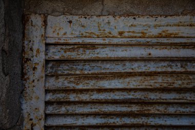 Paslı metal ızgaralar, boyayla boyanmış ve yaşlılıktan soyulmuş, endüstriyel tesislere hava girişi için havalandırma delikleri, bir elektrikli kalkan, bir açık kapı.