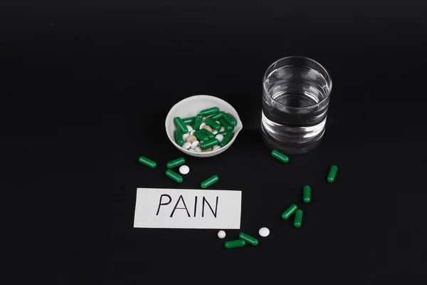 Pillen mit einem Glas Wasser zum Trinken der Pillen auf dunkelschwarzem Hintergrund. Schmerzen — Stockfoto
