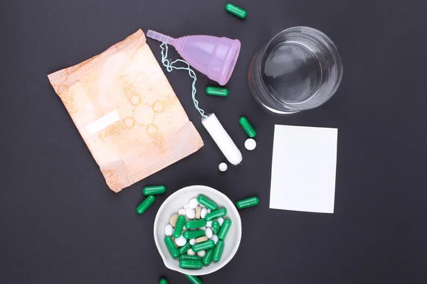 Produtos de higiene feminina com pílulas e água de vidro sobre fundo preto — Fotografia de Stock