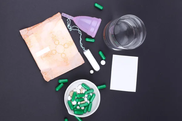 Produtos de higiene feminina com pílulas e água de vidro sobre fundo preto — Fotografia de Stock