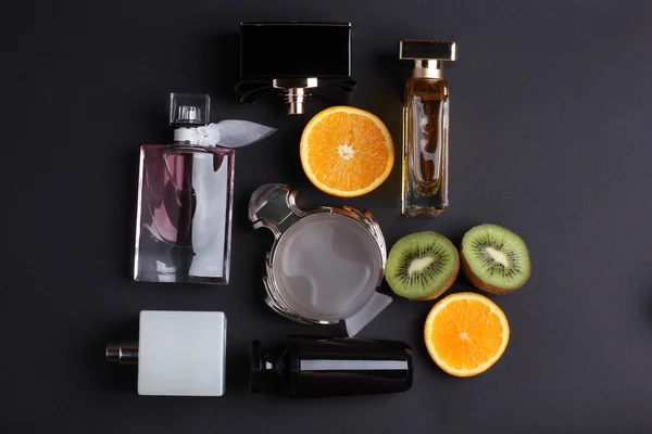 Different perfume bottles with fruit on black background — Stock Photo, Image