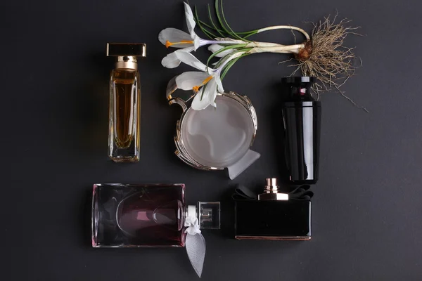 Siyah arka plan üzerine çiçek çevrili parfüm şişeleri. — Stok fotoğraf