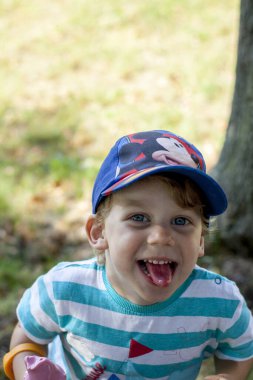 Beyzbol şapkası takan, yaz sıcağında dondurma yiyen sevimli ve gülümseyen küçük bir çocuk..