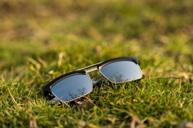 Güneşli bir günde çimlerin üzerinde gümüş lensli klasik güneş gözlüğü modeli çekiliyor. Seçici odak