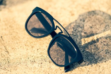 Güneşli bir günde siyah lensli ve siyah çerçeveli güneş gözlükleri dışarıda çekiliyor. Seçici odak