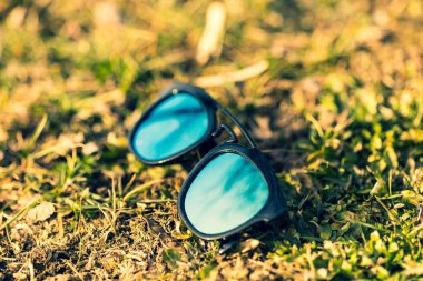 Güneşli bir günde çimlerin üzerinde mavi lensli güneş gözlüğü modeli çekiliyor. Seçici odak