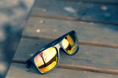 Altın lensli klasik güneş gözlüğü tasarımı bir yaz günü yakın plan çekimde dışarıda çekiliyor. Seçici odak