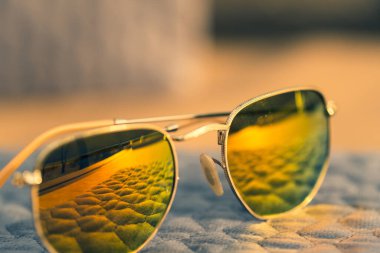 Yuvarlak altın mercekli klasik güneş gözlüğü mankeni bir yaz günü yakın planda dışarıda çekim yapıyor. Seçici odak