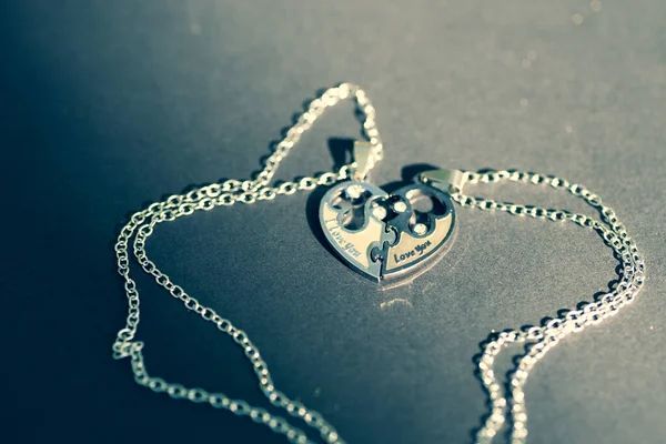 Couple set pendant necklace two half of a heart shoot outdoors in a sunny day closeup. Selective focus — Stock Photo, Image