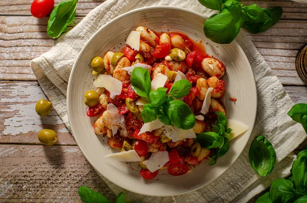 Delicious and simple food, homemade gnocchi with tomato sauce, parmesan, olives and basil