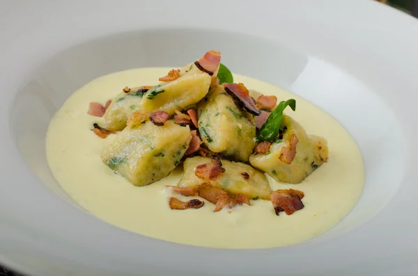 Spinach gnocchi with parmesan sauce topped with bacon — Stock Photo, Image