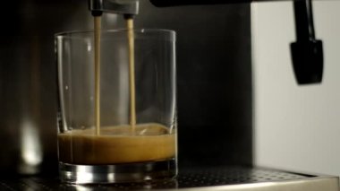 Kahve makinesinden cam bir kaba kahve döküldü.