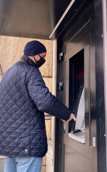 Man met een zwart masker en een wegwerphandschoen gebruikt een pinautomaat. — Stockfoto