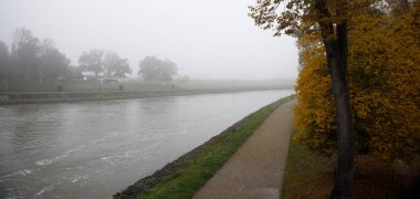 Sisli bir sonbahar sabahında, nehrin kıyısındaki parkta terk edilmiş bir yol.