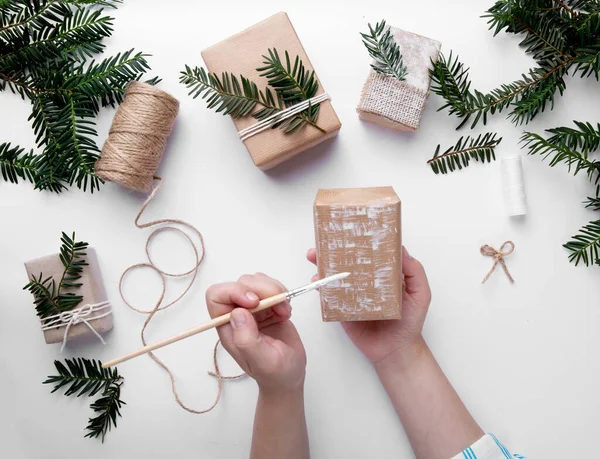 Las manos sostienen un regalo de Navidad y lo decoran con pintura blanca en el escritorio — Foto de Stock