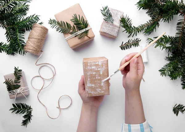 Las manos sostienen un regalo de Navidad y lo decoran con pintura blanca en el escritorio — Foto de Stock