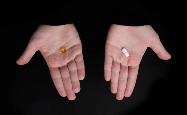 Omega 3 kapsülü ve siyah arka planda iki avuç içi haplı.