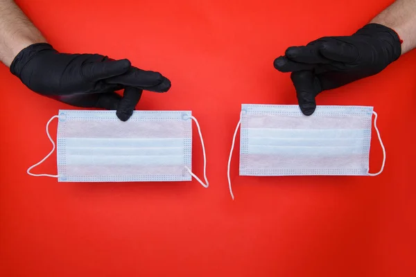 戴黑色胶乳手套的双手拿着两个医用口罩，一个带着撕破的弹力带 — 图库照片