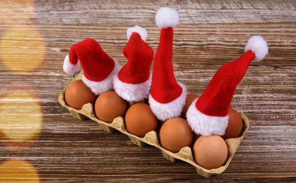 Dozen eggs are on a wooden table and they are wearing Santa hats — Stock Photo, Image