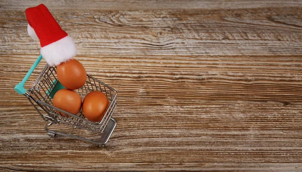 Miniature grocery cart with chicken eggs and little Santa hat — Stock Photo, Image