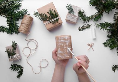 Eller bir Noel hediyesini tutar ve onu beyaz boyayla süsler. 