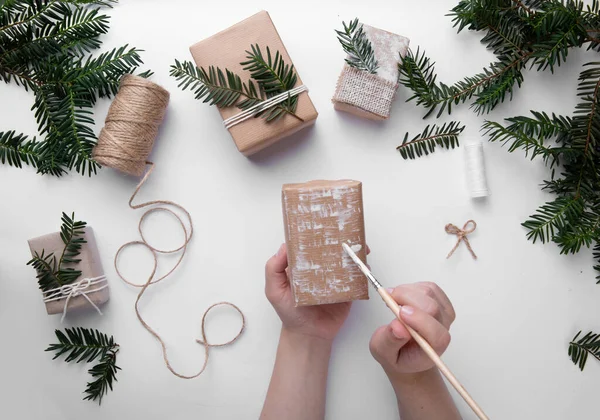 Eller bir Noel hediyesini tutar ve onu beyaz boyayla süsler. 