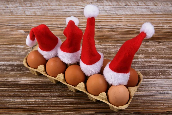 Packaging of chicken eggs in red Santa Claus hats for paper on wooden table — Stock Photo, Image