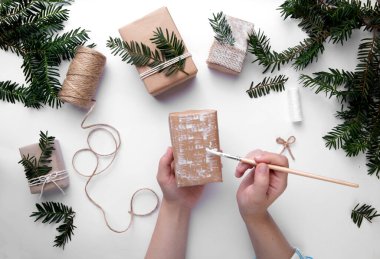 Eller bir Noel hediyesini tutar ve onu beyaz boyayla süsler. 