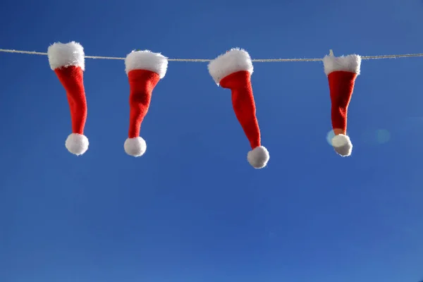 Mavi gökyüzüne karşı ipte sallanan 4 küçük Noel Baba şapkası. yakın plan
