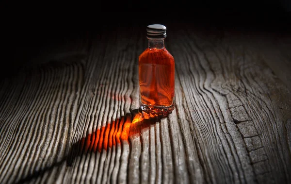 Piccola bottiglia di bevanda rossa nel buio semi sul tavolo di legno. — Foto Stock