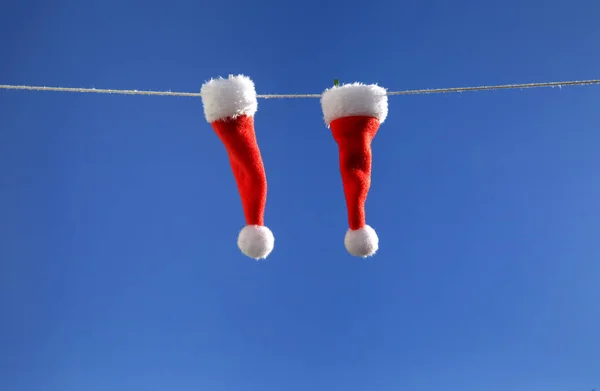 Mavi gökyüzüne karşı ipte sallanan iki küçük Noel Baba şapkası. yakın plan