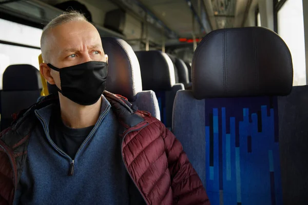 L'uomo viaggia su un treno indossando una maschera nera sotto restrizioni sanitarie Foto Stock Royalty Free
