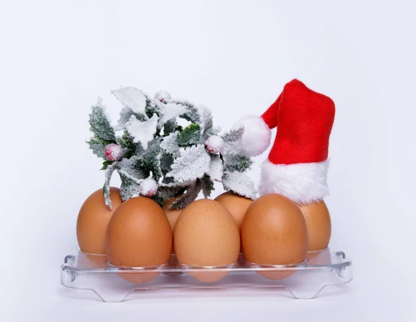 Chicken eggs on a tray from the refrigerator Santa hat and Christmas twig — Stock Photo, Image