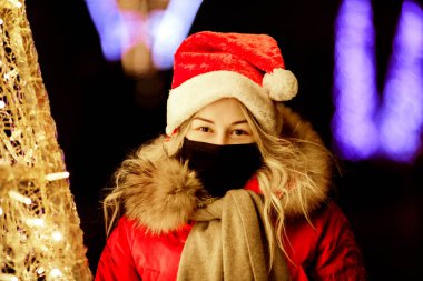Siyah maskeli genç kız, Noel Baba şapkası ve yeni yıl aydınlanması. 