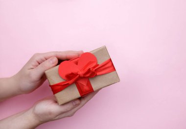 Kırmızı kurdeleli hediye kutusu ve pembe arka planda kadın ellerinde fiyonk