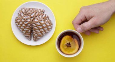 Bir fincan kokulu meyve çayı ve çay tabağında taze zencefilli ekmek tutan bir erkek.