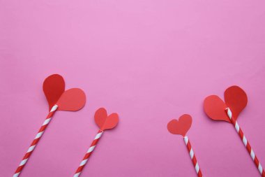 Tepesinde pembe arka planda kırmızı kağıt kalpler olan dört çizgili tüp.