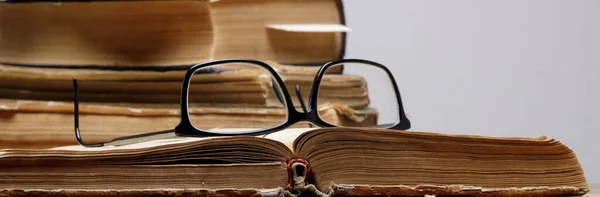 Tahta masa üzerinde kitap ayracı olan bir yığın eski kitap. Gözlükler açık bir kitabın üzerinde..