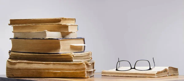  Masada bir yığın eski kitap ve okuma gözlüğü duruyor.