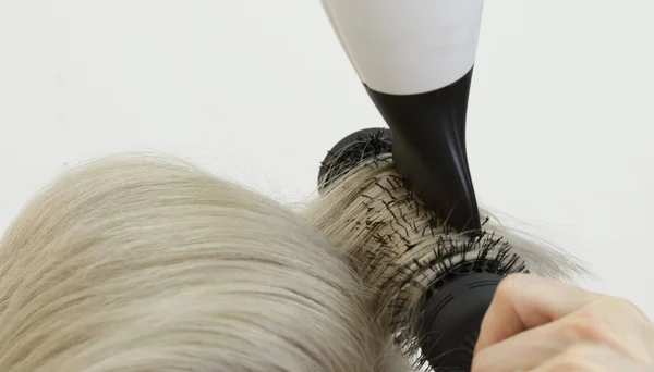 Cabeleireiro invisível mãos linha o cabelo modelo loiro usando secador de cabelo e pente — Fotografia de Stock