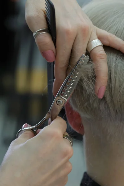 Beautiful hairdresser hands hold scissors and comb and cut the model hair