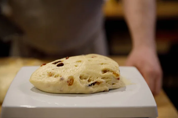 Un morceau de pâte avec des raisins secs repose sur les échelles culinaires pour mesurer — Photo