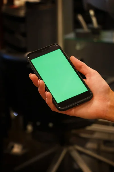 De menselijke hand toont een mobiele smartphone met een groen scherm — Stockfoto