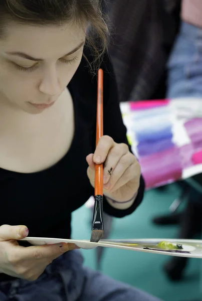 Lány egy paletta festékek és ecsettel rajzolni a kezét a festék — Stock Fotó